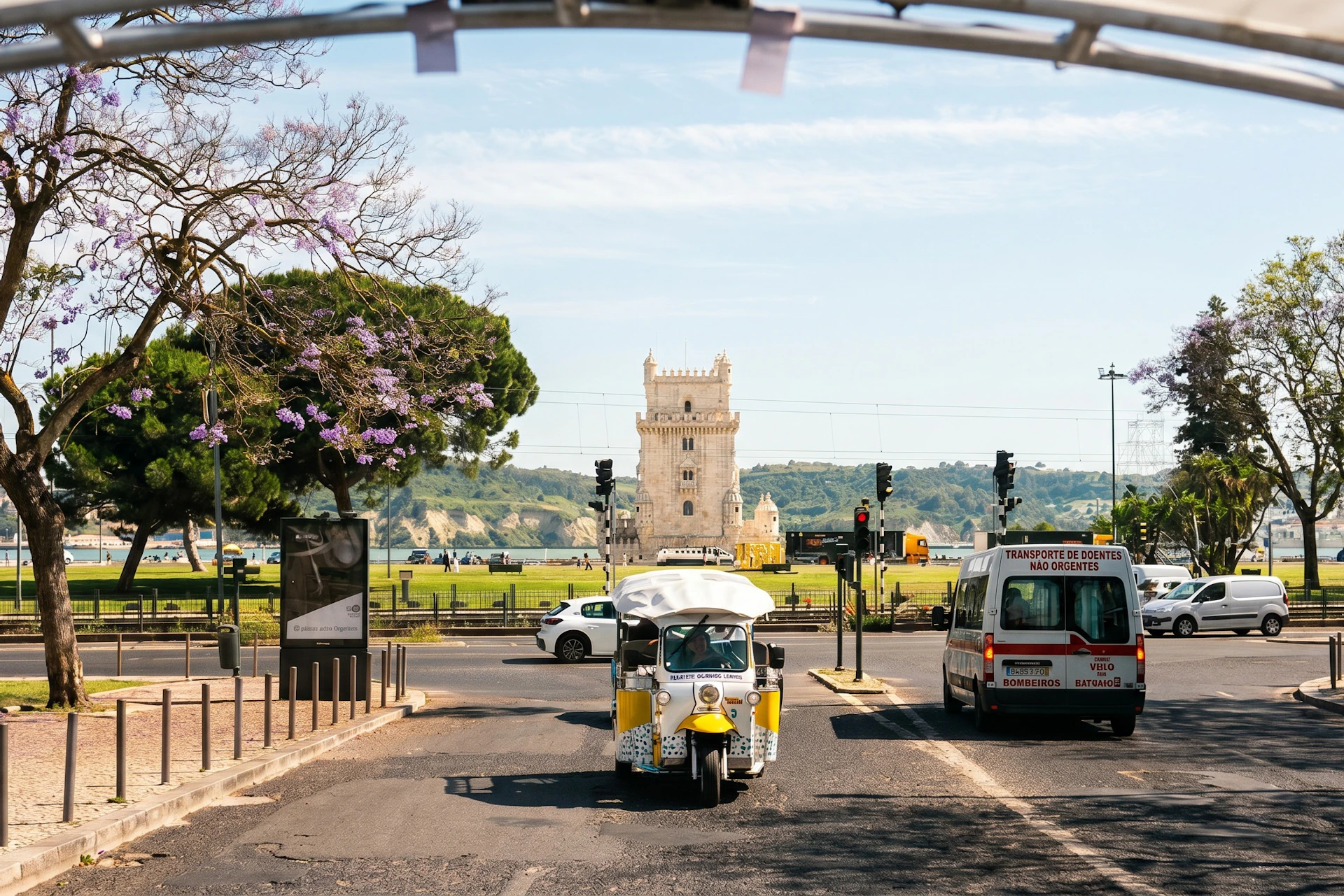 A tuk-tuk and other vehicles on a street with a historic tower in the background during a sunny day.