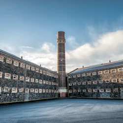 A large brick tower rises between two connected stone buildings under a blue sky with scattered clouds.