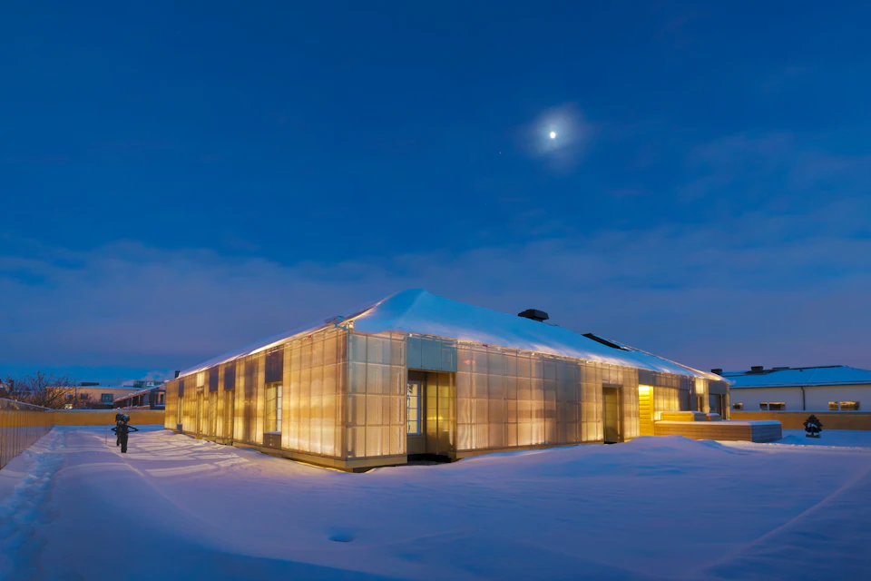 A modern building with illuminated walls stands in a snowy landscape at dusk under a moonlit sky.