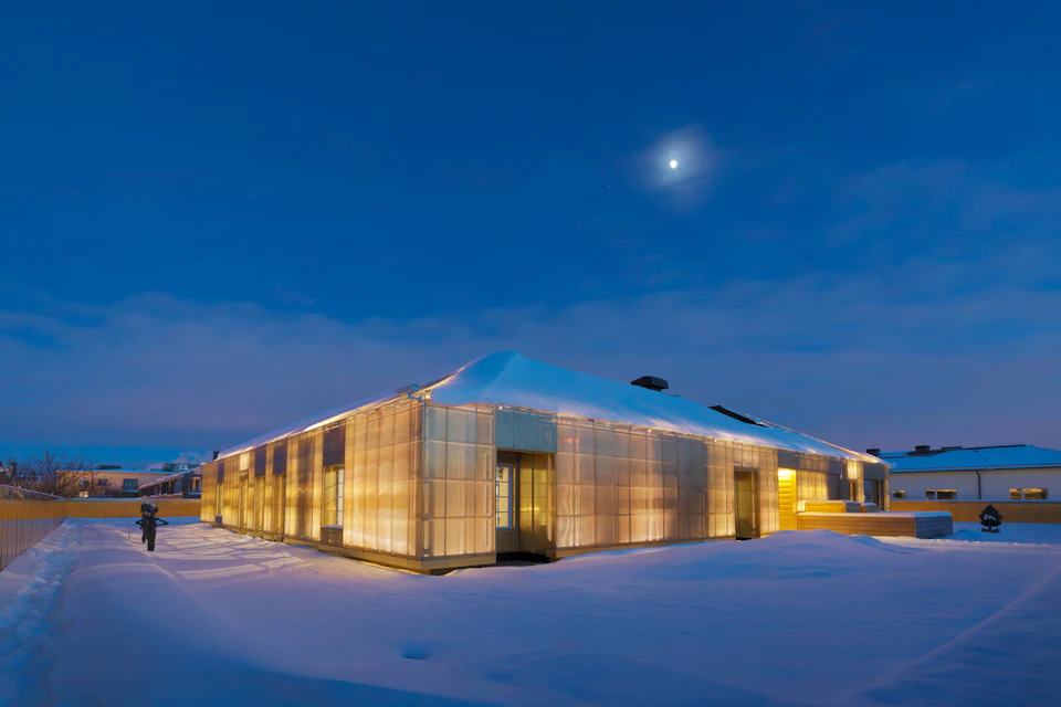A modern building with illuminated walls stands in a snowy landscape at dusk under a moonlit sky.