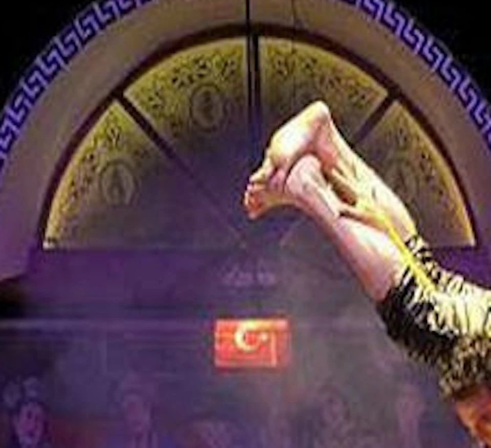 Performers in period costumes on stage; one man lifts another upside down. Audience in the background.
