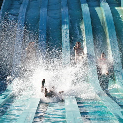 Människor som glider nerför blå vattenrutschbanor med stänk och mycket vatten som sprutar runt dem.