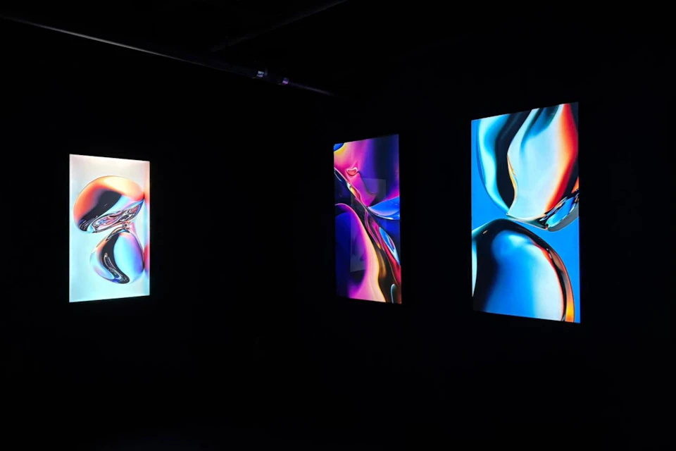 Three vertical abstract artworks with vibrant colors displayed in a dark room.
