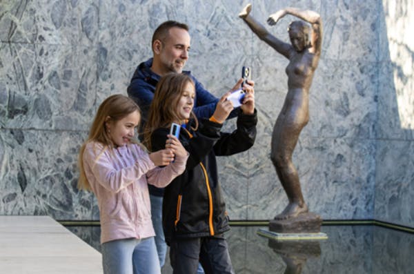 한 남자와 두 명의 어린이가 대리석 벽 앞에 서서 미소를 지으며 카메라나 휴대폰을 들고 사진을 찍는 듯합니다.