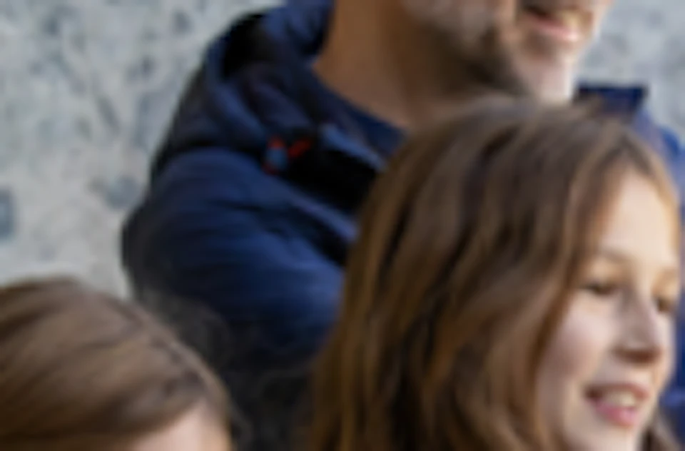 A man and two children stand in front of a marble wall, smiling and holding up cameras or phones as if taking photos.