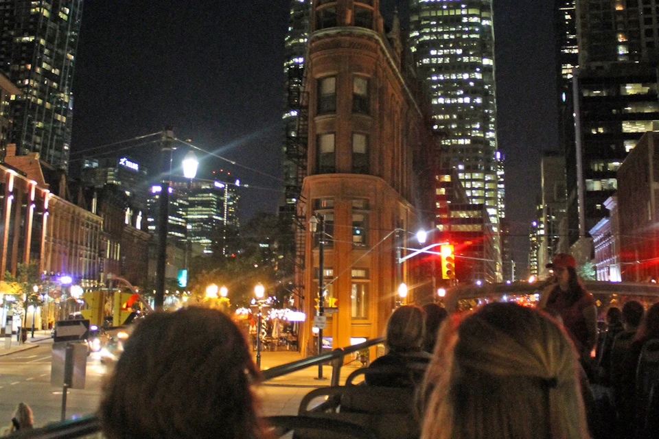 Open top double decker bus tour approaching the Flatiron building in Toronto at night