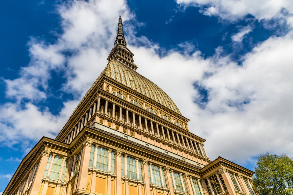 A close-up view of a tall, ornate building with a spire against a partly cloudy blue sky.