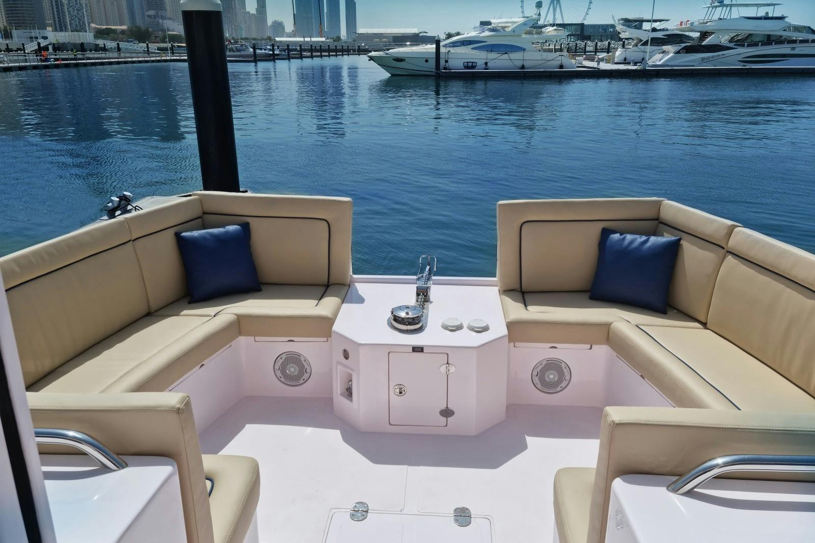 A luxury boat seating area with beige cushions and blue pillows, set against a marina view with yachts and a city skyline.