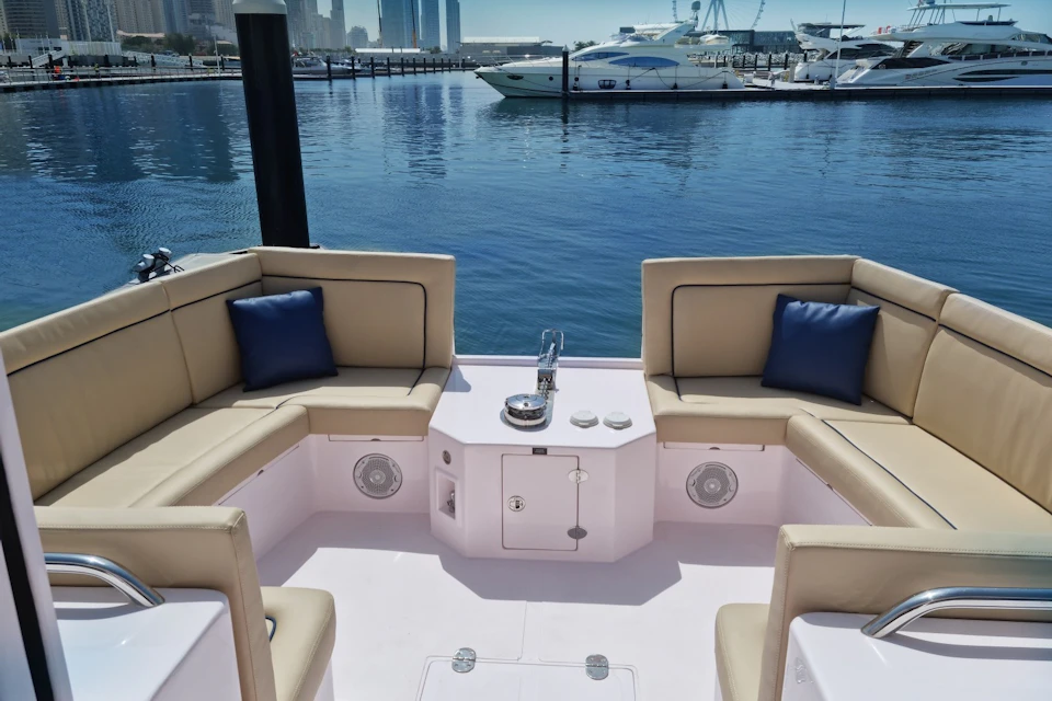 A luxury boat seating area with beige cushions and blue pillows, set against a marina view with yachts and a city skyline.