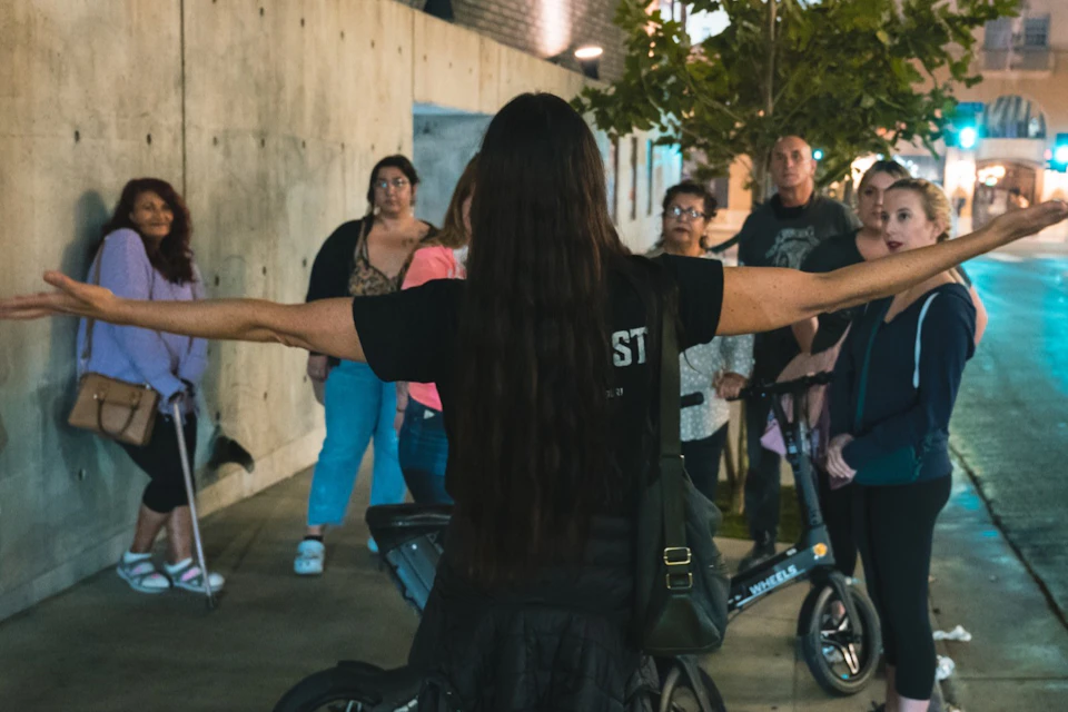Guide standing in front of a crowd with her arms open wide telling a story.