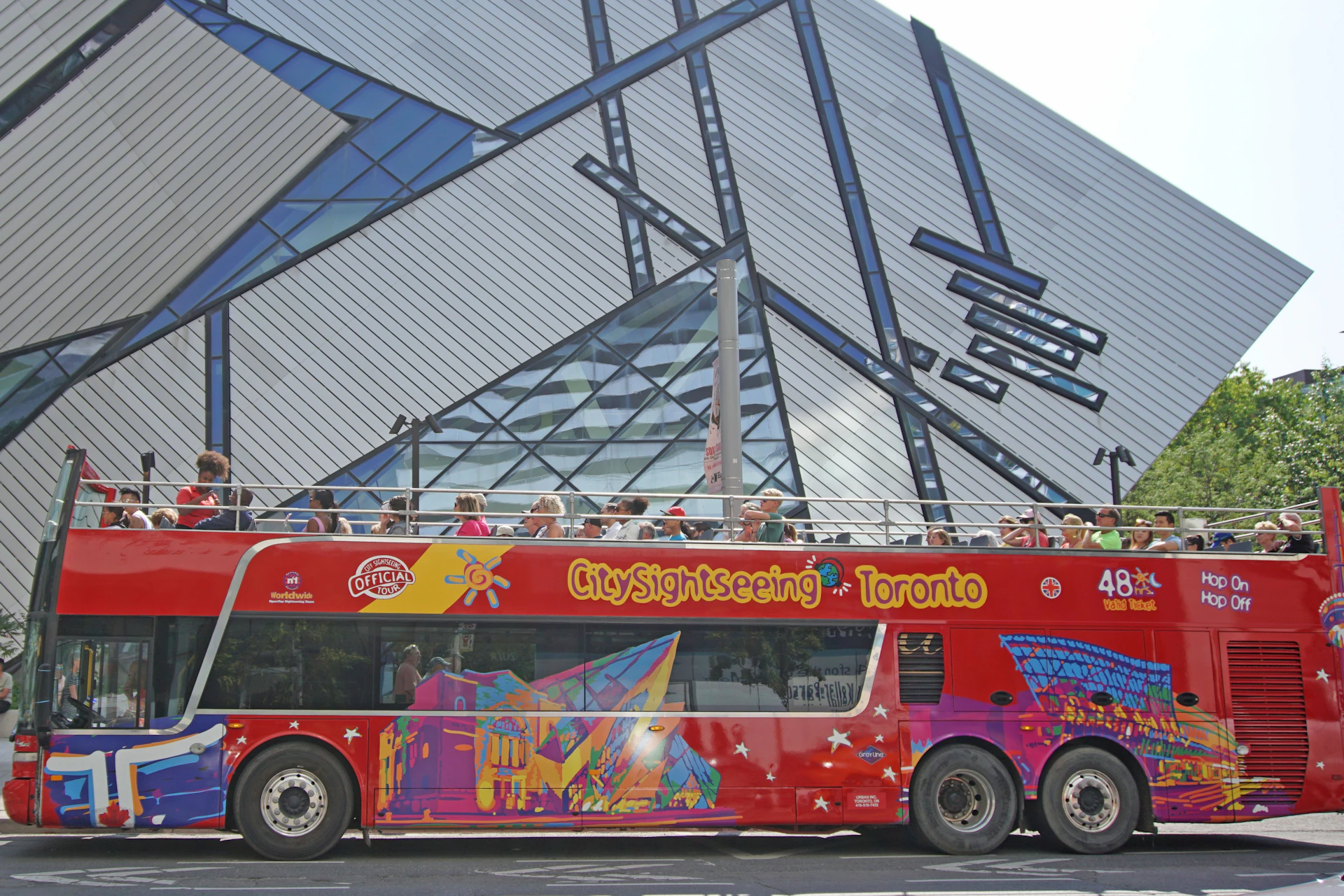 A red double-decker sightseeing bus with the text 'City Sightseeing Toronto,' parked in front of a modern glass building.