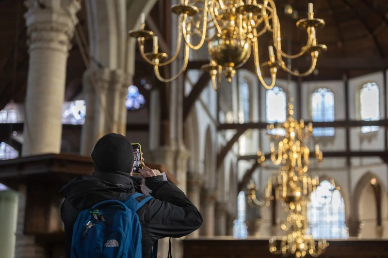 Person with a blue backpack photographing inside a grand cathedral with ornate chandeliers and high arches.