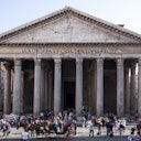 Grande edificio antico con colonne, affollato di persone. L'iscrizione sulla facciata recita: