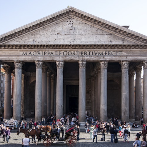 Grande edificio antico con colonne, affollato di persone. L'iscrizione sulla facciata recita: