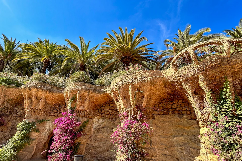 Stone columns with vibrant pink flowers and overhanging palm trees under a bright blue sky.