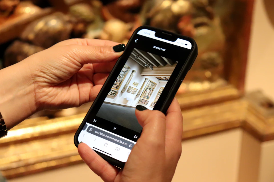 Close-up of hands holding a smartphone displaying an image of an art gallery with paintings on the screen.