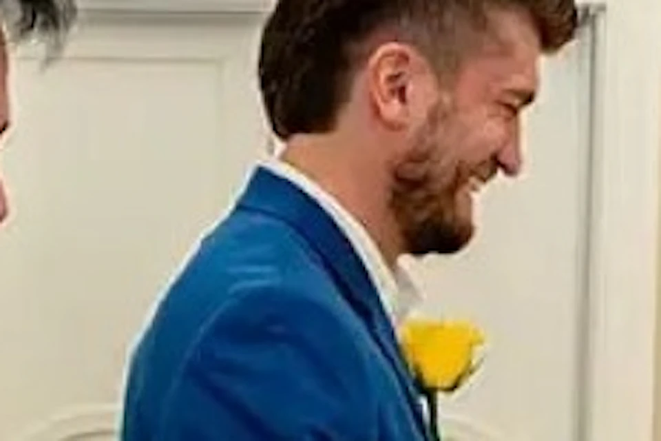 A couple in wedding attire stands facing each other in a chapel, while a man dressed as Elvis Presley poses enthusiastically nearby.