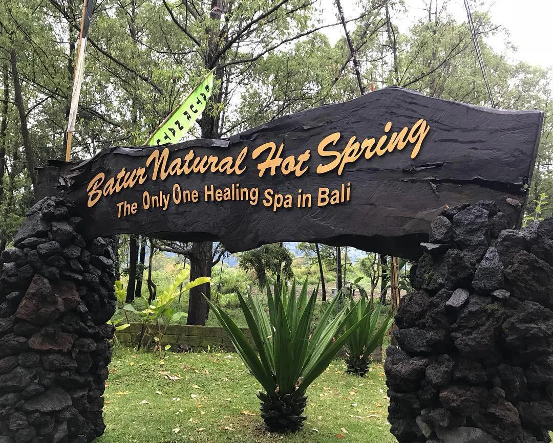 Entrance sign for Batur Natural Hot Spring, reading "The Only One Healing Spa in Bali," surrounded by greenery.