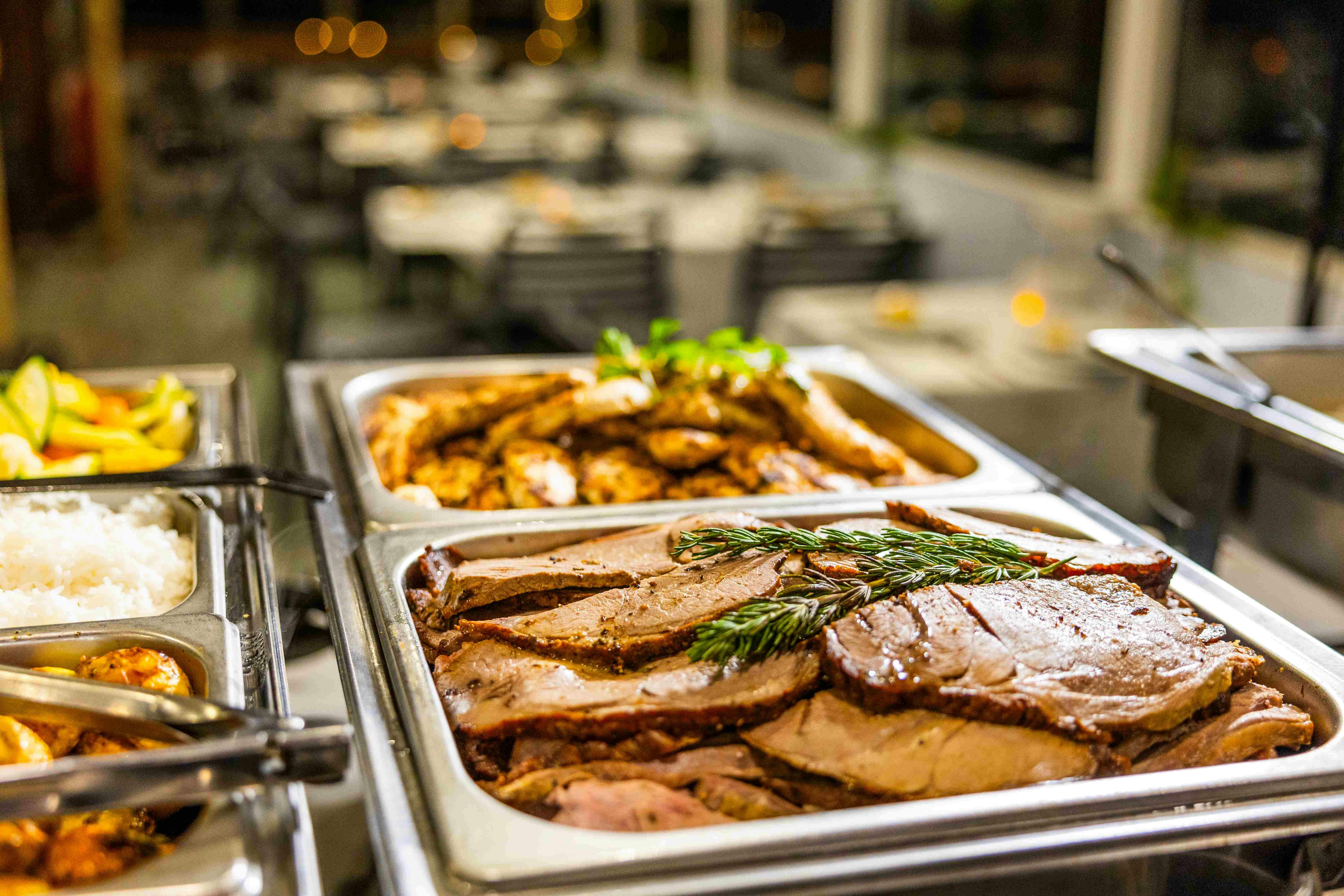 两盘切片肉类，其中一盘点缀香草，自助餐，背景是模糊的用餐区。