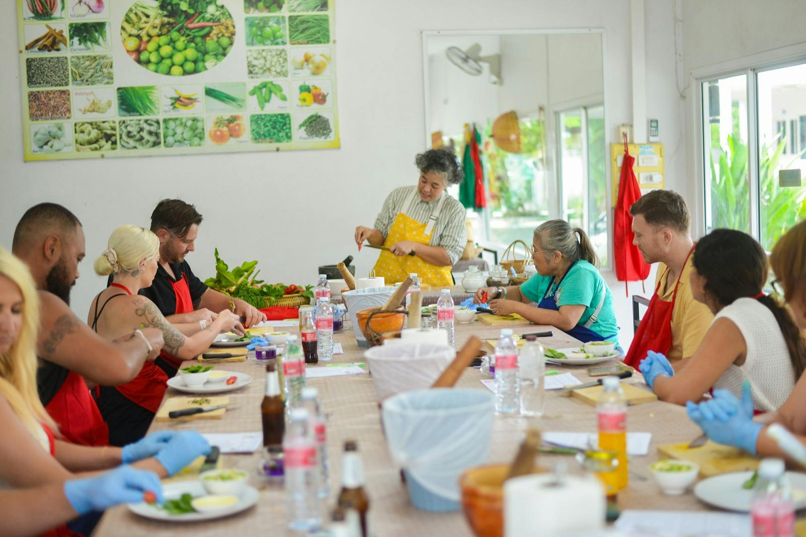 人们围坐在桌子旁准备食物，一个围裙的人在示威。 桌上摆放着各种蔬菜和餐具。