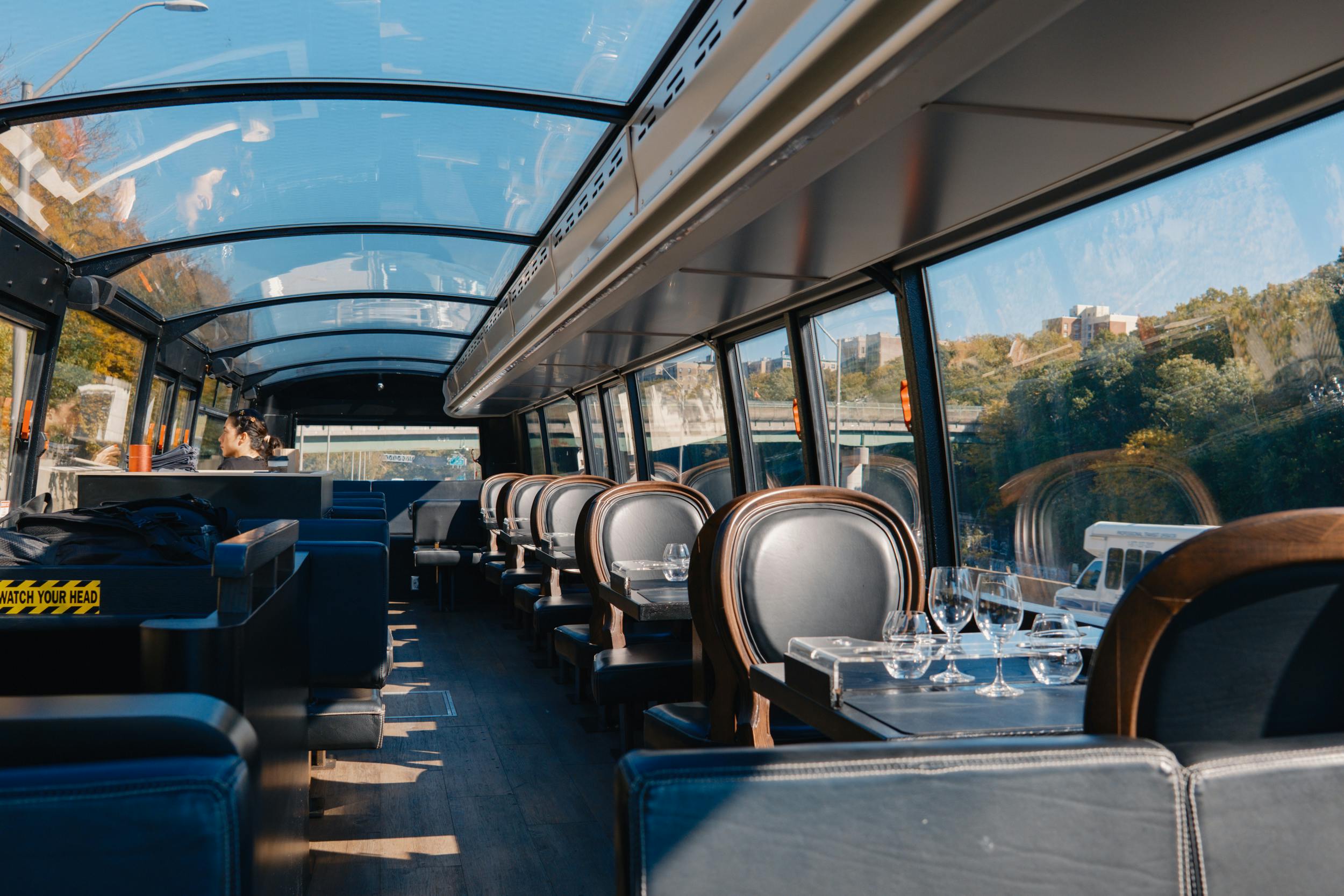 Intérieur d'un wagon-restaurant vide avec toit en verre, sièges bleus et tables garnies de verres, surplombant un paysage verdoyant.