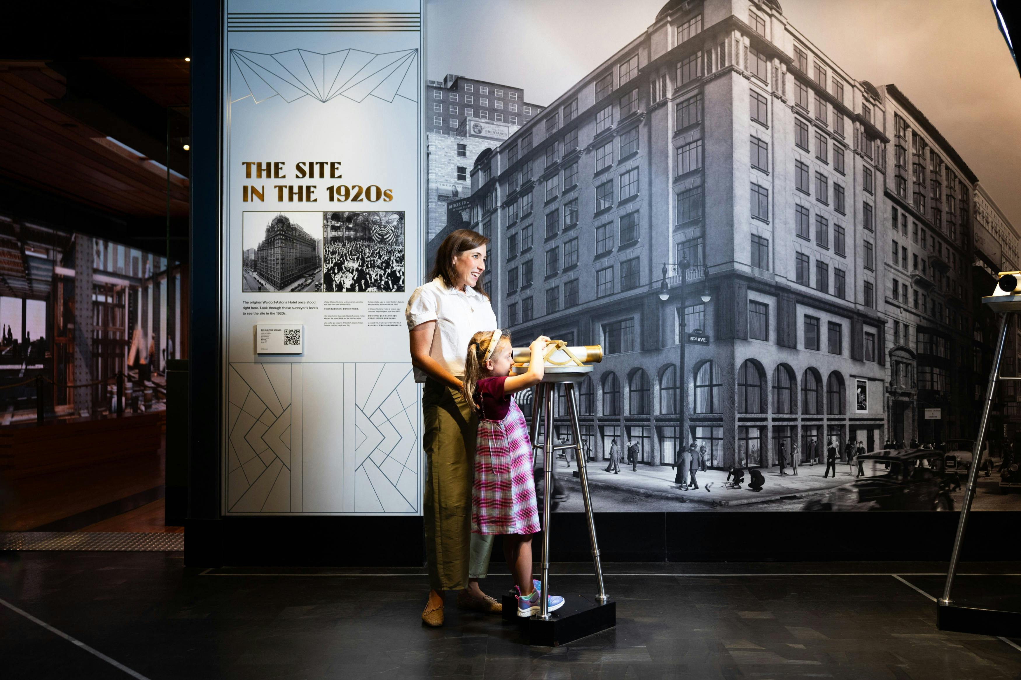 Una donna e un bambino interagiscono con un display davanti a una mostra storica che presenta una grande immagine in bianco e nero di un paesaggio urbano degli anni '20.