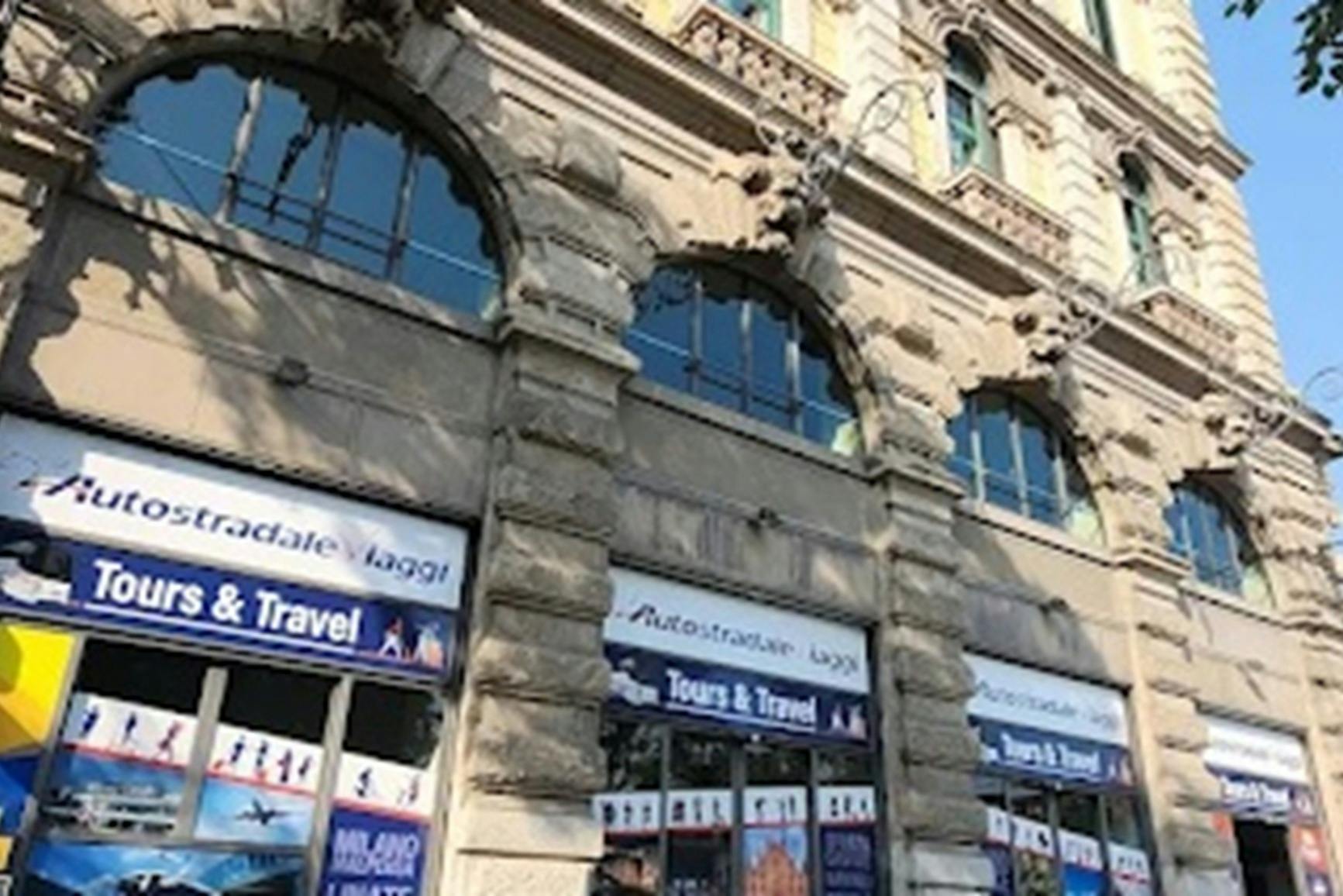 Facade of a stone building with arched windows and travel agency signage on the ground floor.