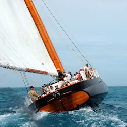 A sailboat with several people on board leans to the side, cutting through the blue water. The boat's name, "America 2.0," is visible.