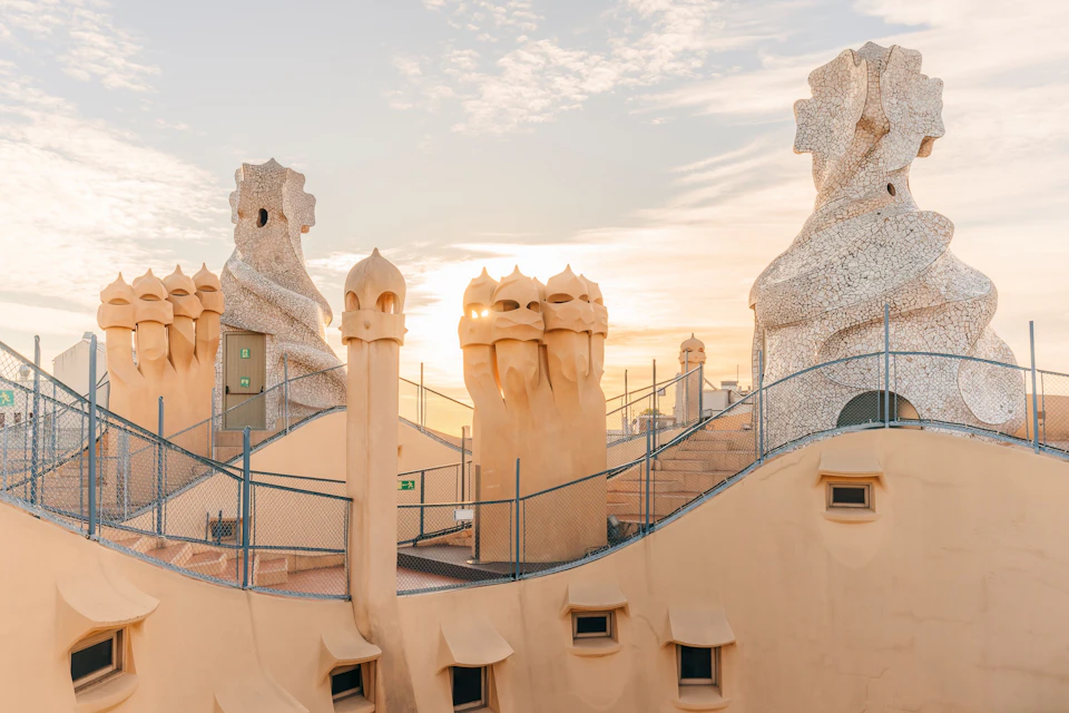 A rooftop with sculptural chimneys and curving designs under a sky at sunset.
