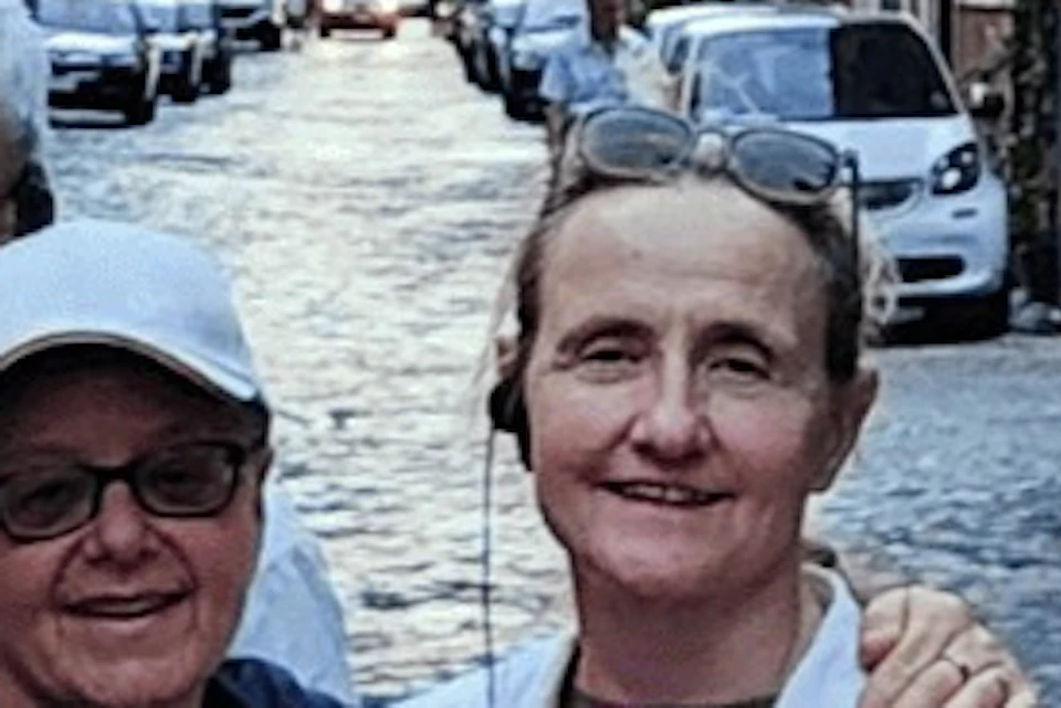 A group of five people posing on a cobblestone street lined with parked cars and historic buildings in the background.