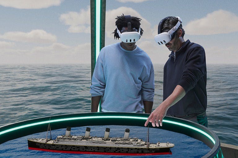 Dva lidé s VR náhlavními soupravami komunikují s digitálním modelem lodi na kruhovém displeji na pozadí oceánu.