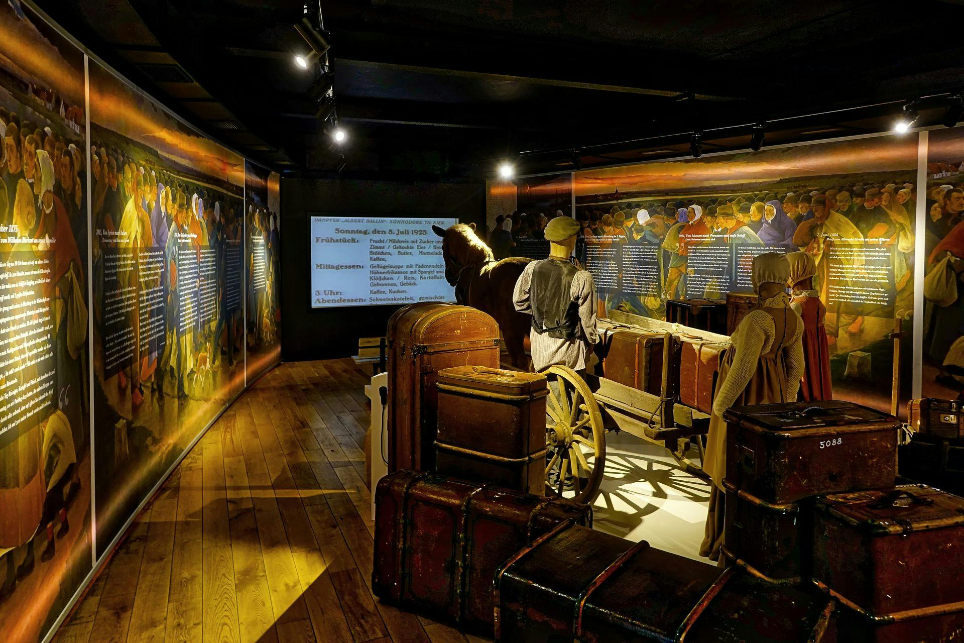 Utställning med skyltdockor i tidstypiska kläder med vagn och bagage. Väggar visar historisk text och bilder under svag belysning.
