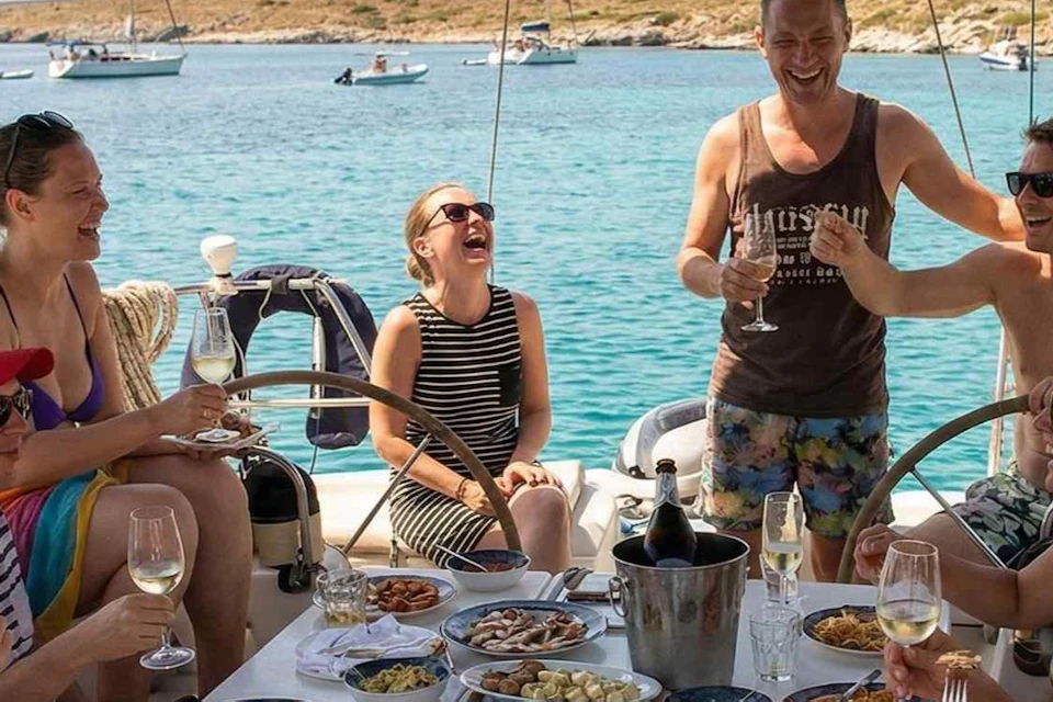 A group of people enjoying a meal and drinks on a boat with a scenic ocean view in the background.