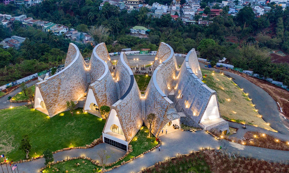 Aerial view of a modern architectural building with curved, illuminated structures surrounded by greenery and a small town.