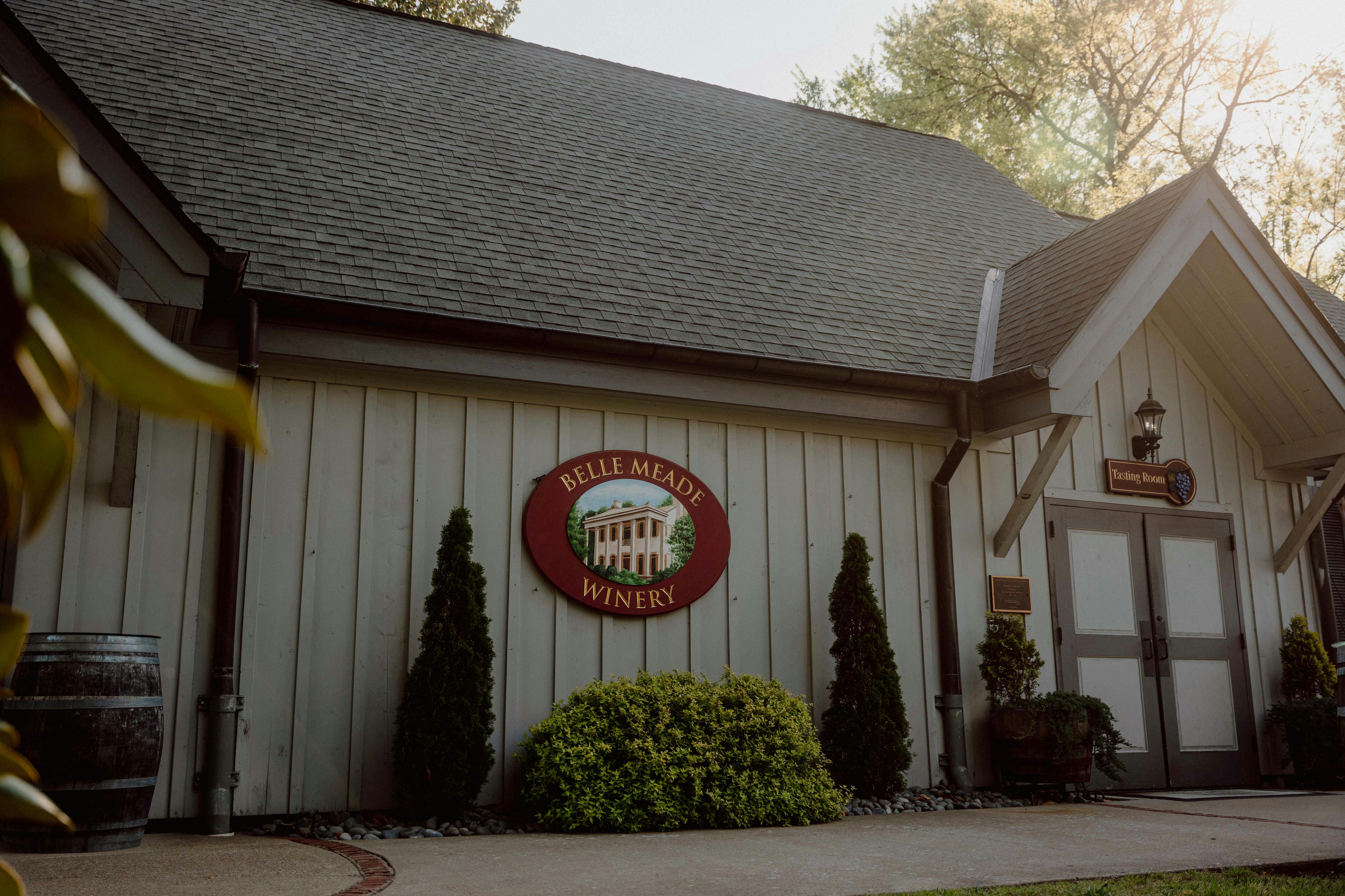 Exteriér Vinařství Belle Meade zdobí nápis, zeleň a stromy v pozadí pod jasnou oblohou.