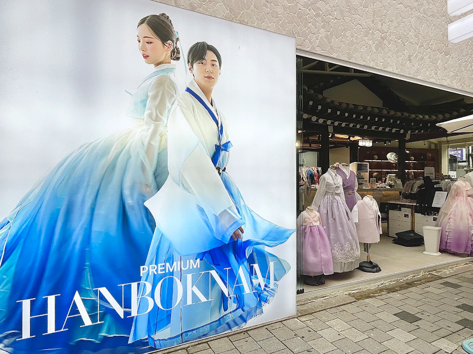 A storefront display featuring a poster of two individuals in traditional blue and white Korean hanbok attire.