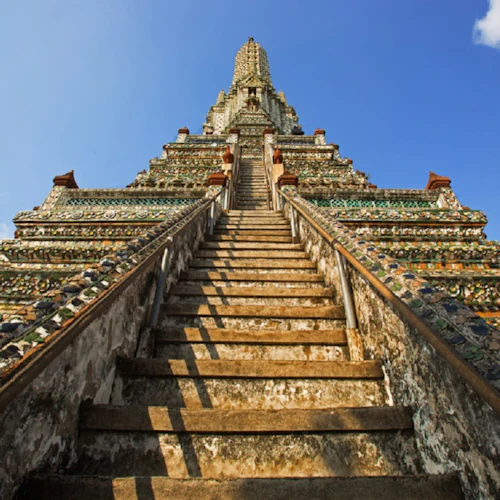 Eine steile Steintreppe, die zu einem kunstvoll verzierten, alten Tempel führt, vor einem strahlend blauen Himmel.