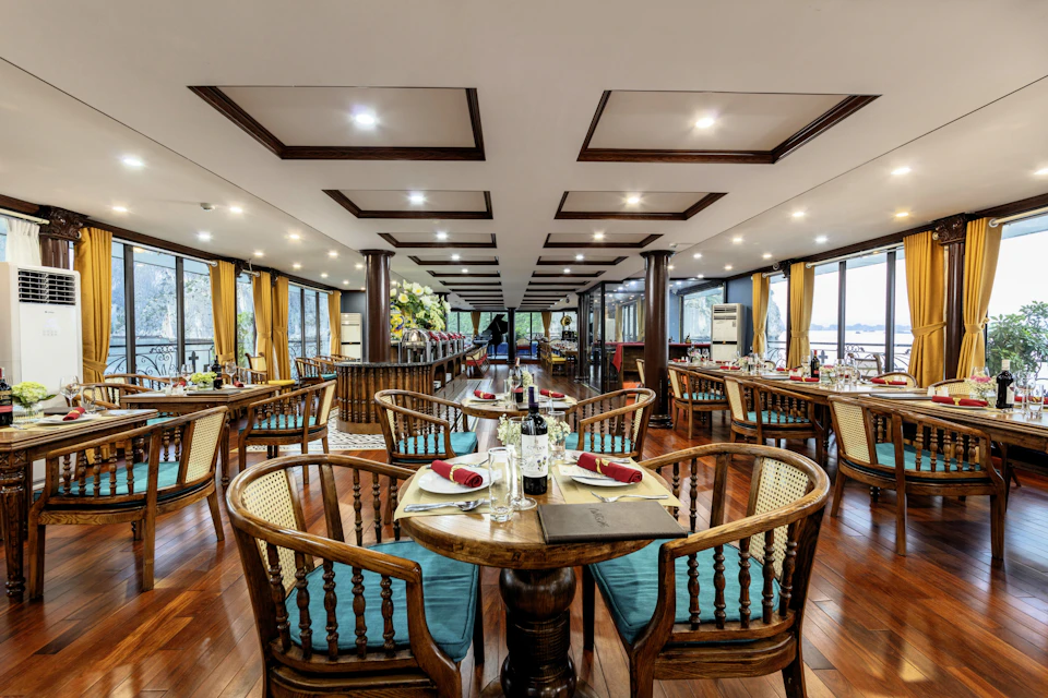 A dining room with wooden chairs and tables set with dishes and wine bottles, featuring large windows and a polished floor.