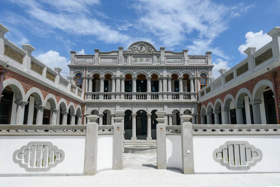 A two-story classical-style building with arches and columns, set against a blue sky with light clouds.