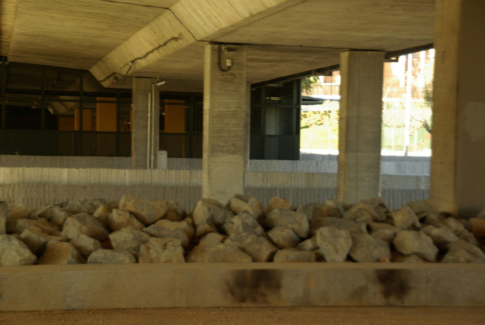 지반을 따라 커다란 암석이 쌓여 있고 천장을 받치고 있는 구조 기둥이 있는 콘크리트 지하 통로.