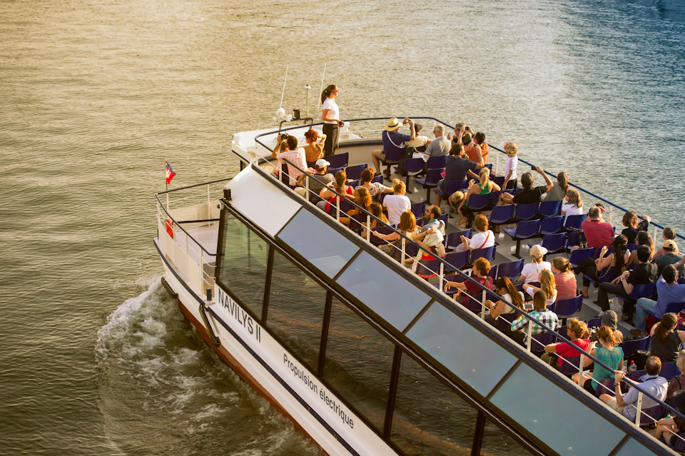 A boat named "NAVILYS II" with many passengers seated, cruising on a river under clear weather.