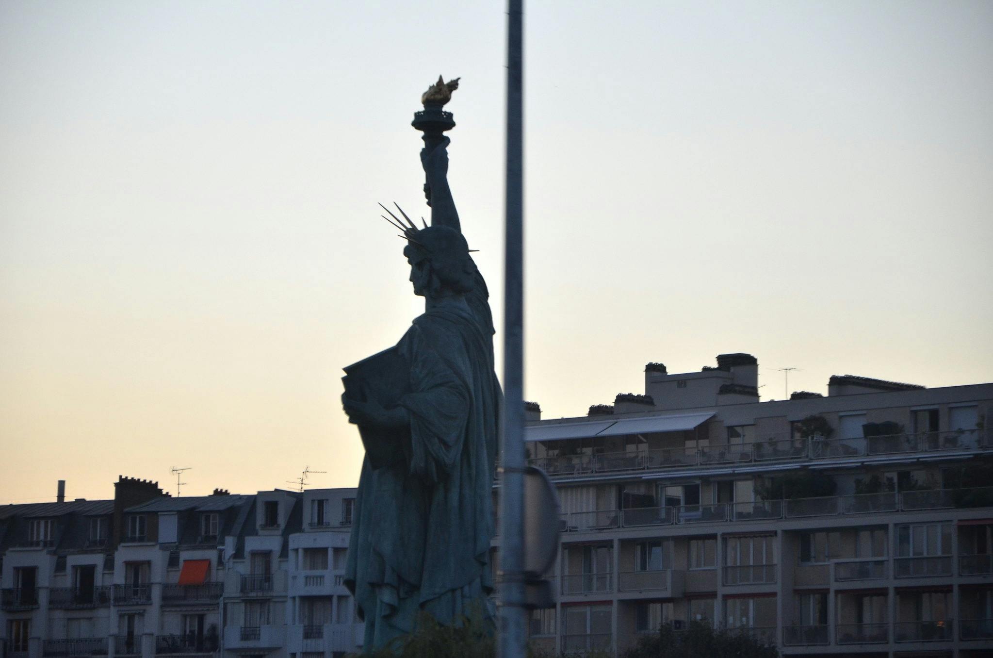 Σιλουέτα ενός αντιγράφου του Αγάλματος της Ελευθερίας με πολυκατοικίες στο παρασκήνιο το σούρουπο.