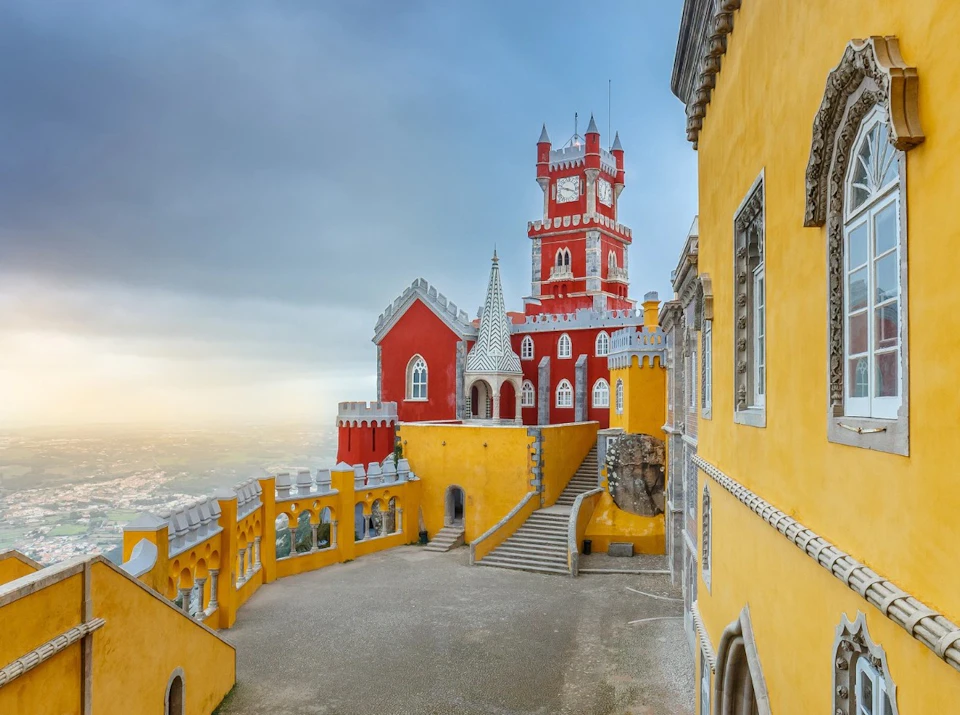 A courtyard with colorful yellow and red castle buildings featuring towers under a cloudy sky.