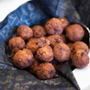 A pile of fried, golden-brown arancini balls resting on dark, patterned napkins in a white bowl.