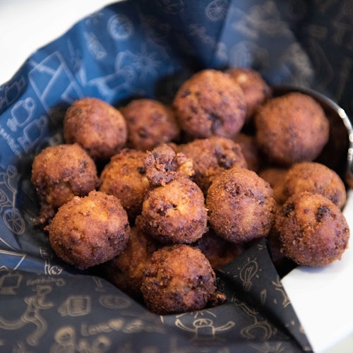 A pile of fried, golden-brown arancini balls resting on dark, patterned napkins in a white bowl.