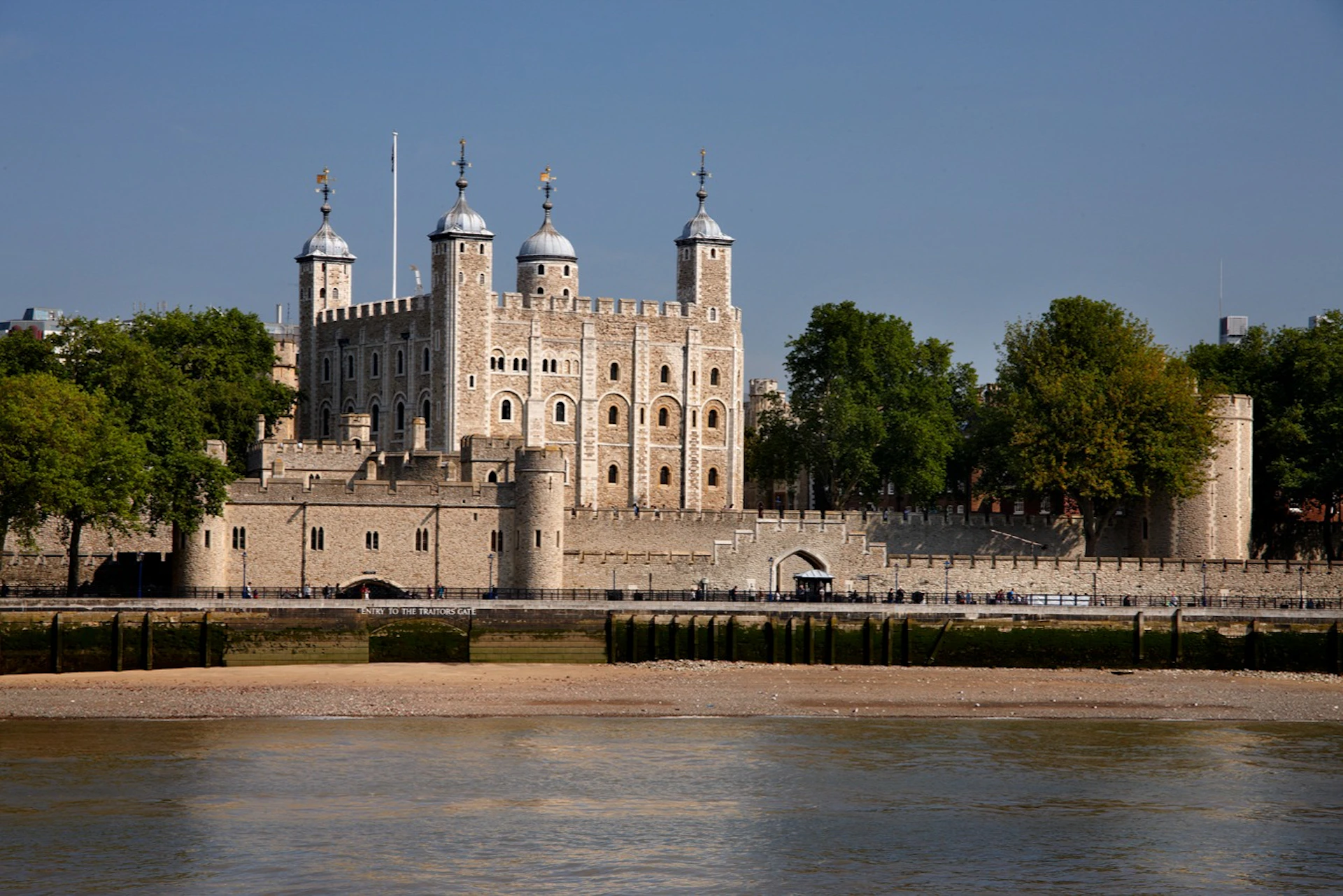 Historic stone fortress with turrets and battlements, located beside a river with trees in the background under a clear sky.