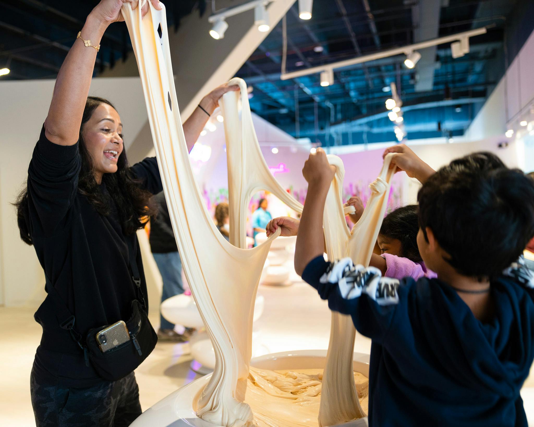 Folk strækker store stykker dejlignende materiale i et indendørs rum med lys belysning og moderne indretning.