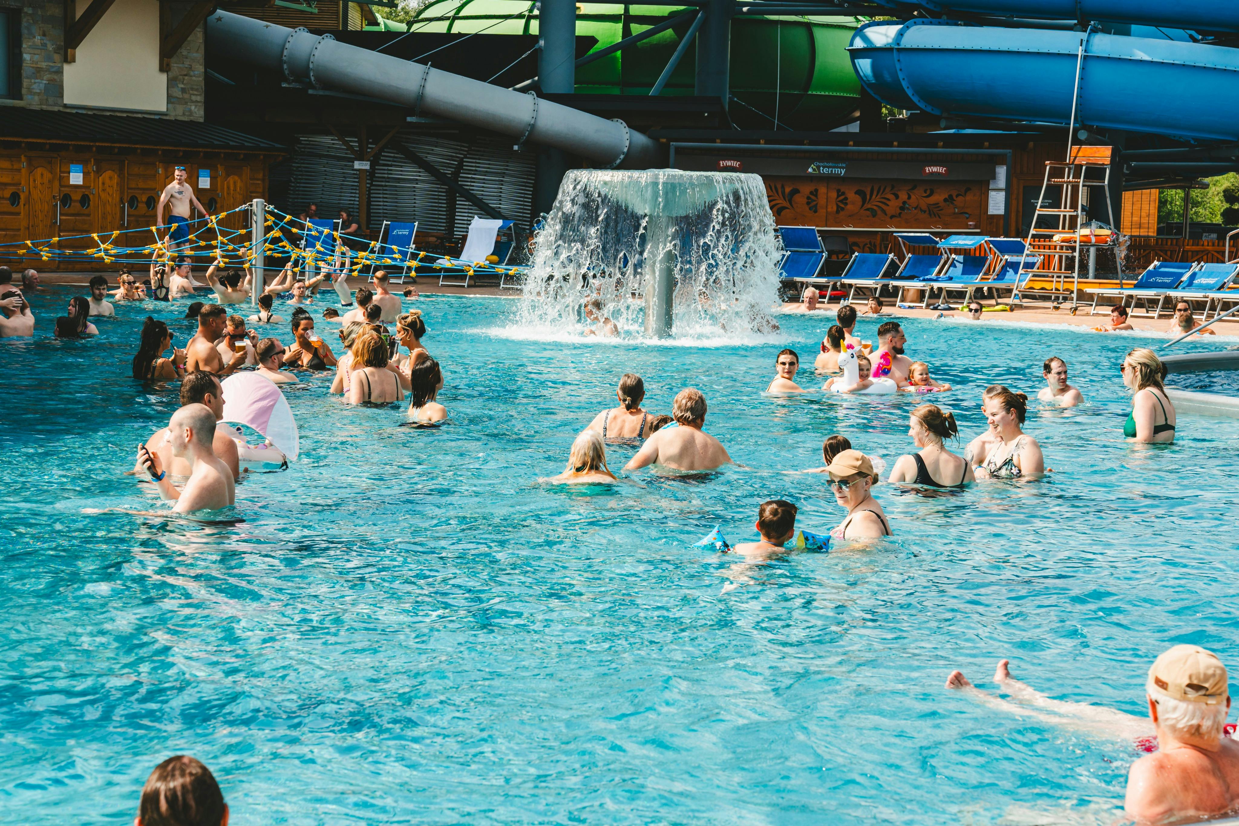 中央の滝の周りには、人々が水を楽しんでいる混雑したプールがあります。 ウォータースライダーをバックに。