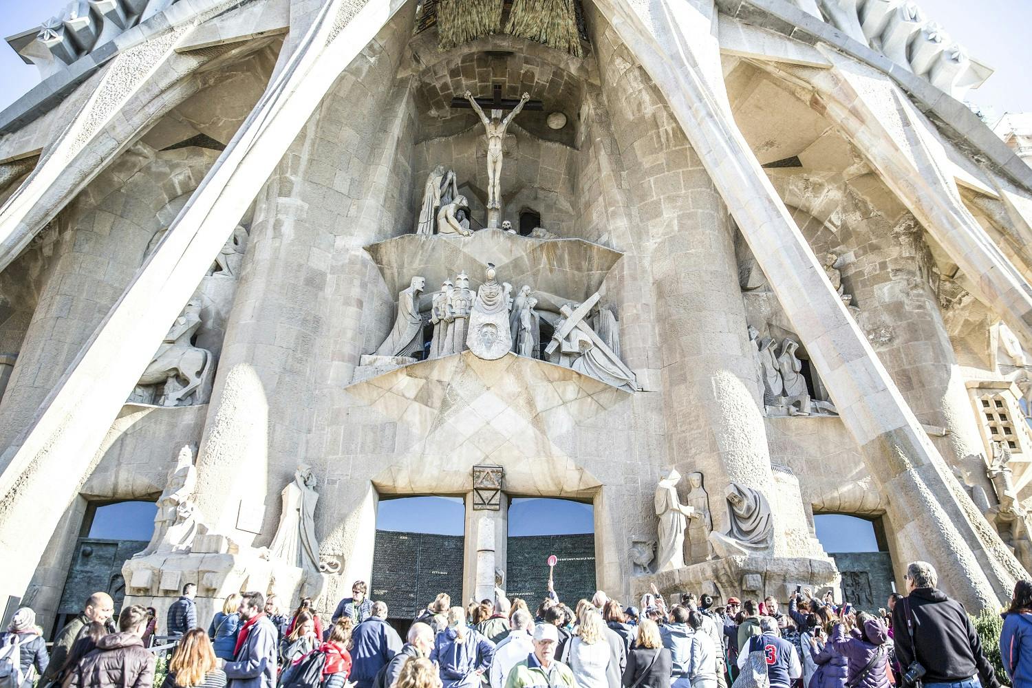 Crowd standing in front of a detailed stone facade adorned with religious sculptures, including a crucifixion scene.