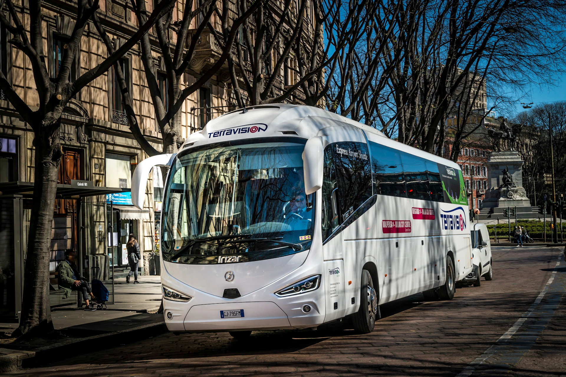 A white tour bus marked with 'Terravision' parked on a street lined with leafless trees and buildings.